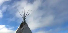 Top of a teepee with clouds and blue sky in the background